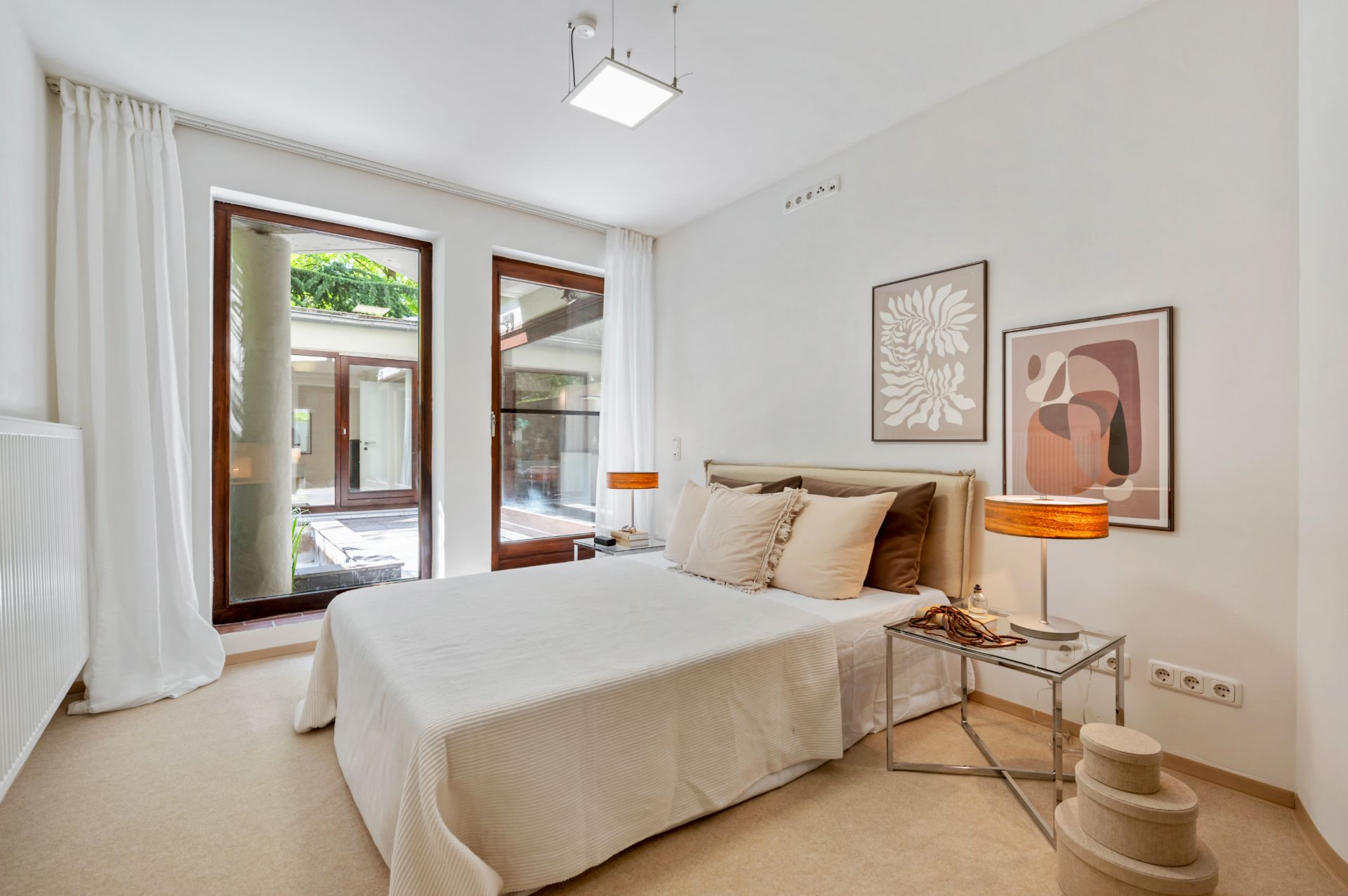Helles Schlafzimmer mit Doppelbett, Nachttisch und großen Fenstern, moderne Kunst an der Wand.
