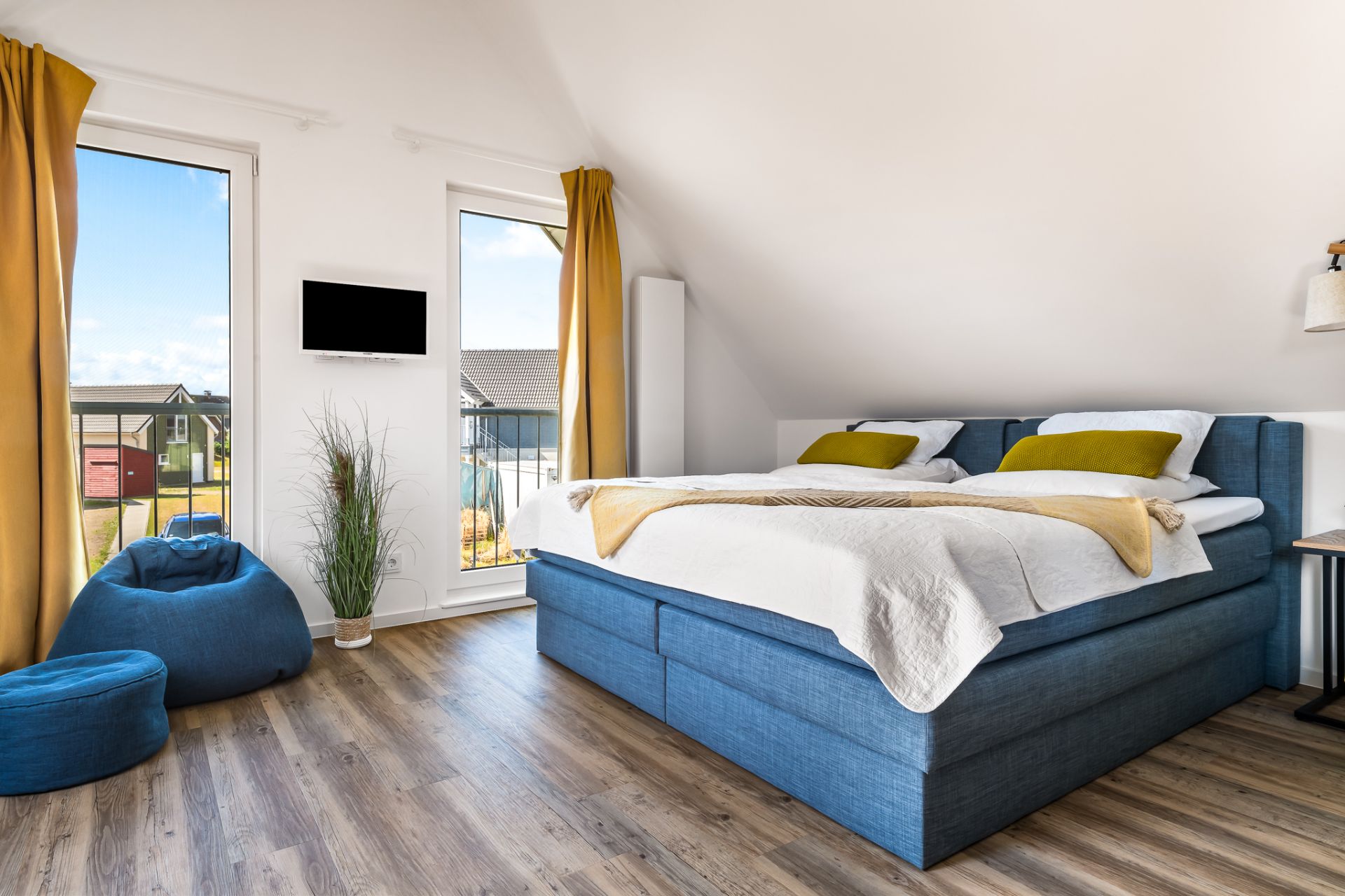 Modernes Schlafzimmer mit blauem Bett, gelben Vorhängen und zwei Fenstern mit Ausblick.