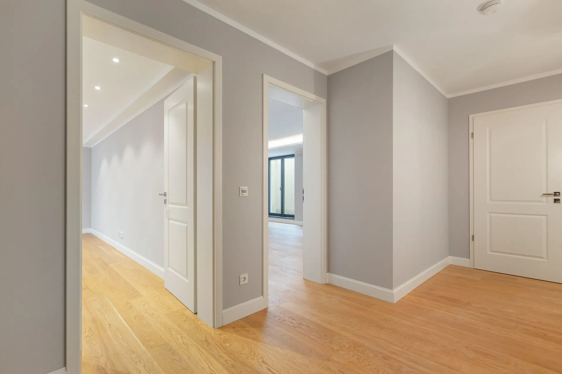 Heller Flur mit Holzboden, drei weißen Türen und grauen Wänden in einer Wohnung.