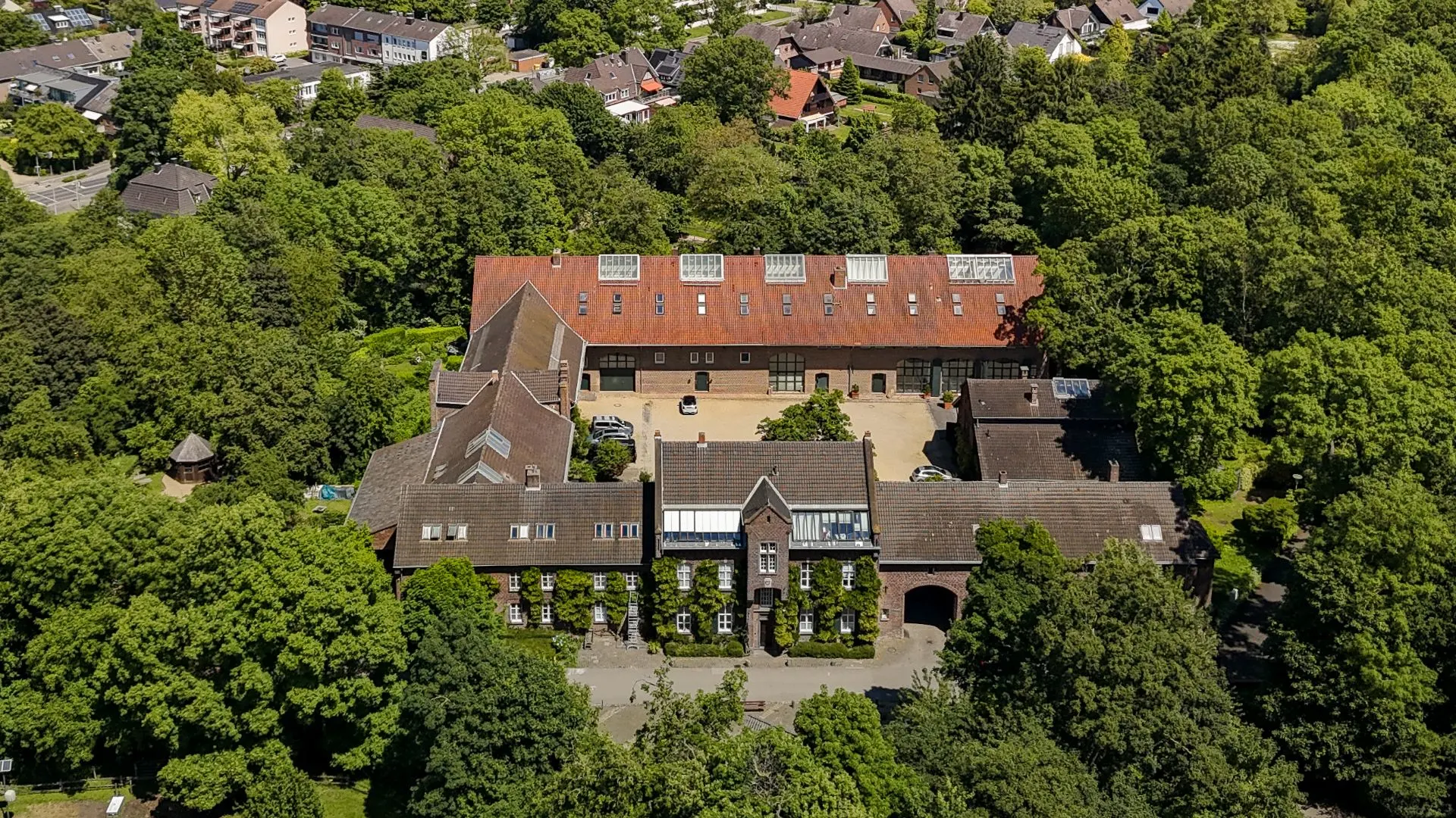 Luftaufnahme eines großen Wohngebäudes mit Innenhof, umgeben von vielen Bäumen.