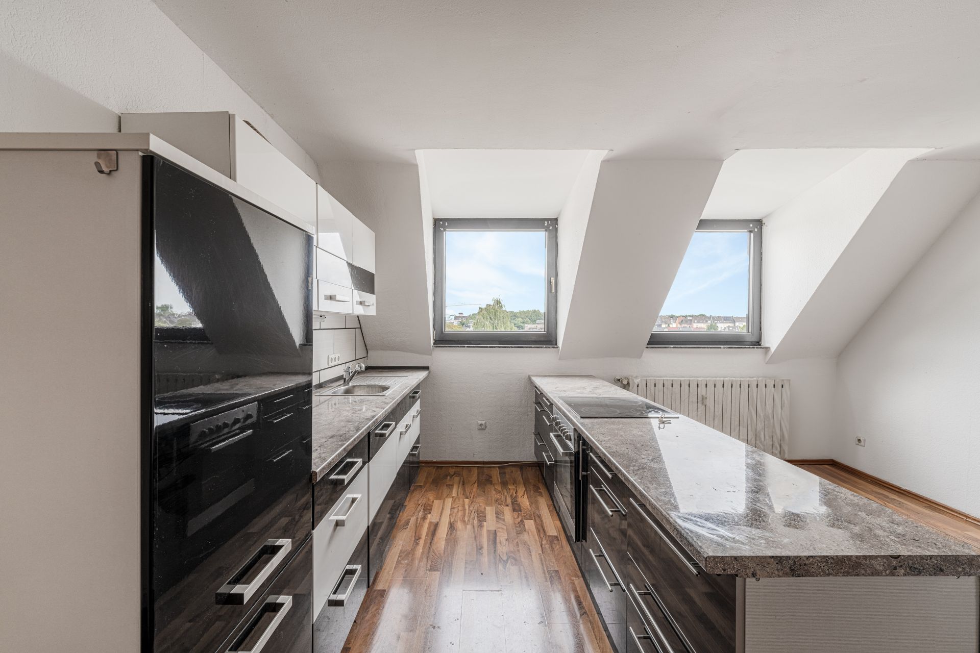 Moderne Einbauküche mit zwei Fenstern, dunklen Fronten und Arbeitsplatten aus Stein.