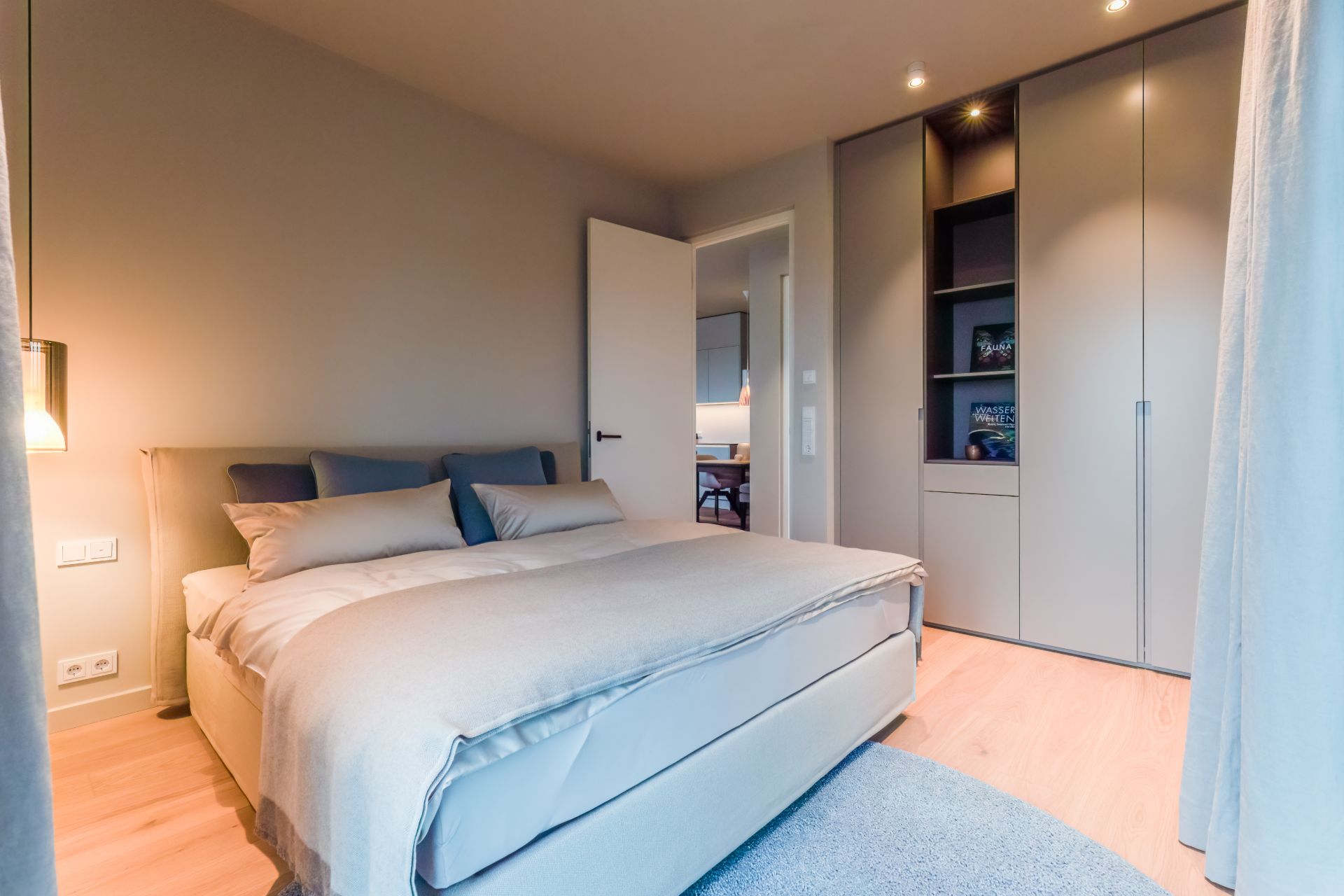 Modernes Schlafzimmer mit Doppelbett, Einbauschrank und offen stehender Tür.