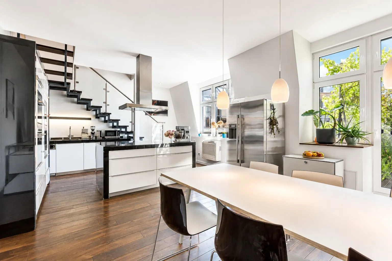 Moderne Küche mit Esstisch, Holzfußboden, großen Fenstern und offener Treppe.