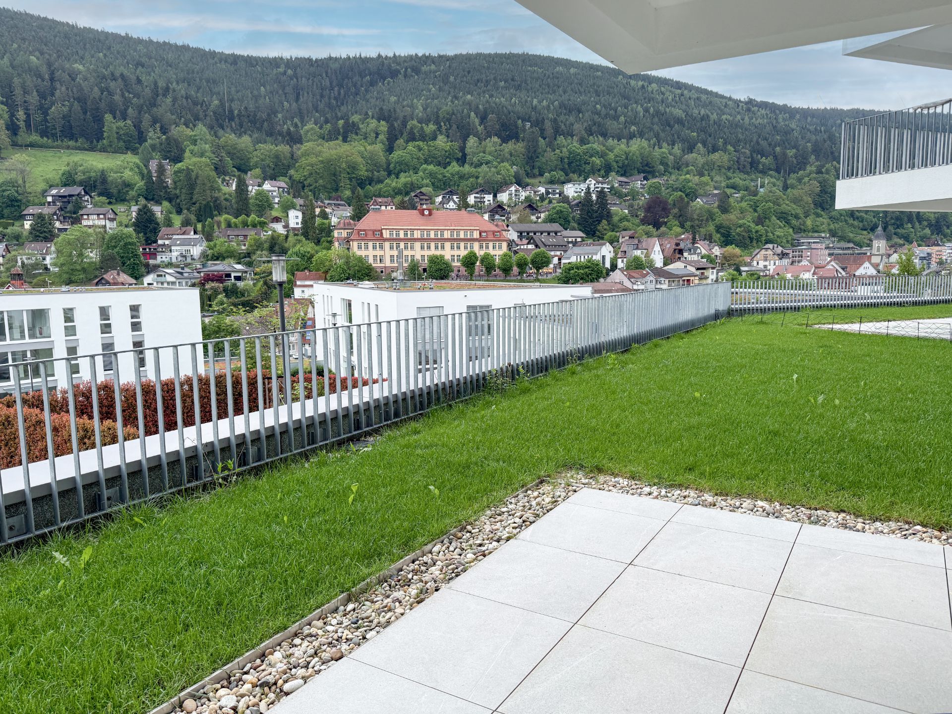 Grüne Terrasse mit Blick auf Hügel, Bäume und Häuser eines Wohngebiets.