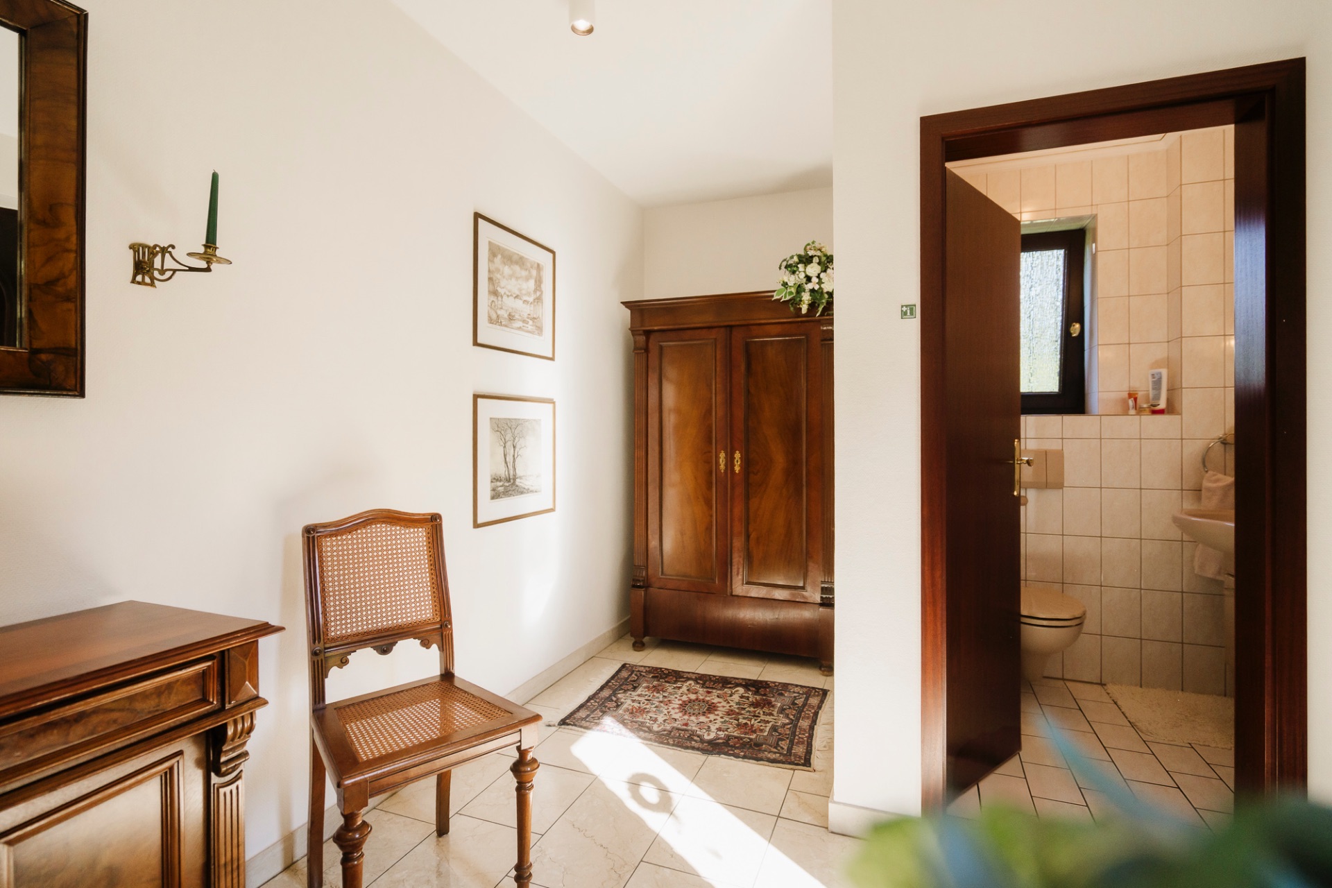 Flur mit Holzmöbeln, Teppich und Blick in ein kleines, gefliestes Badezimmer mit Fenster.