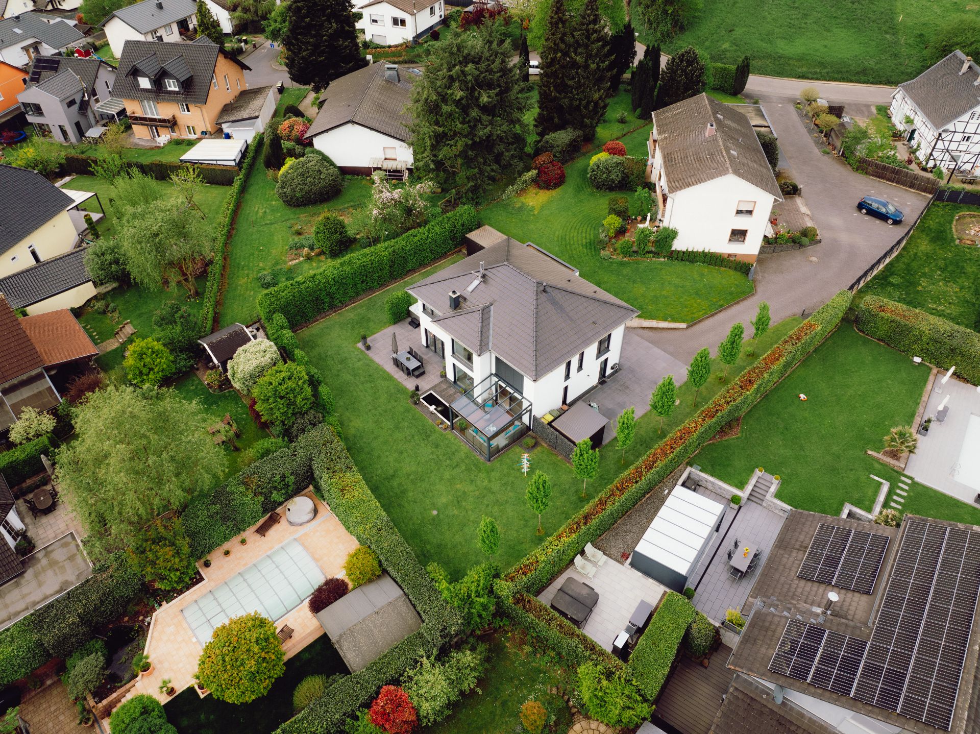 Luftaufnahme eines Einfamilienhauses mit großem Garten und Terrasse in einer Wohnsiedlung.