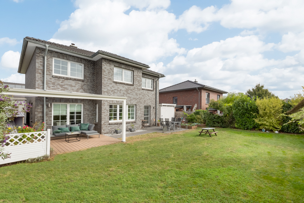 Zweistöckiges Haus mit Terrasse, Gartenmöbeln und weitläufigem Rasen im Garten.
