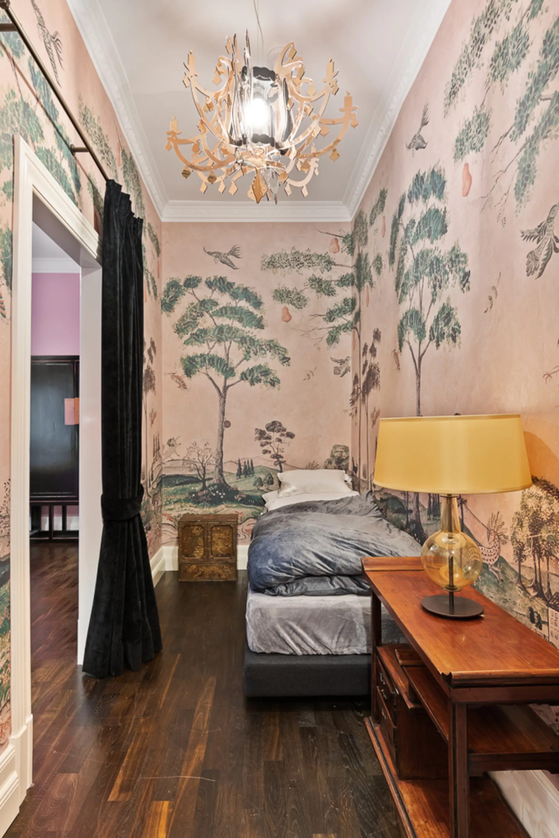 Kleines Schlafzimmer mit Tapete im Baum- und Vogelmotiv, Einzelbett, Nachttisch und Lampe.