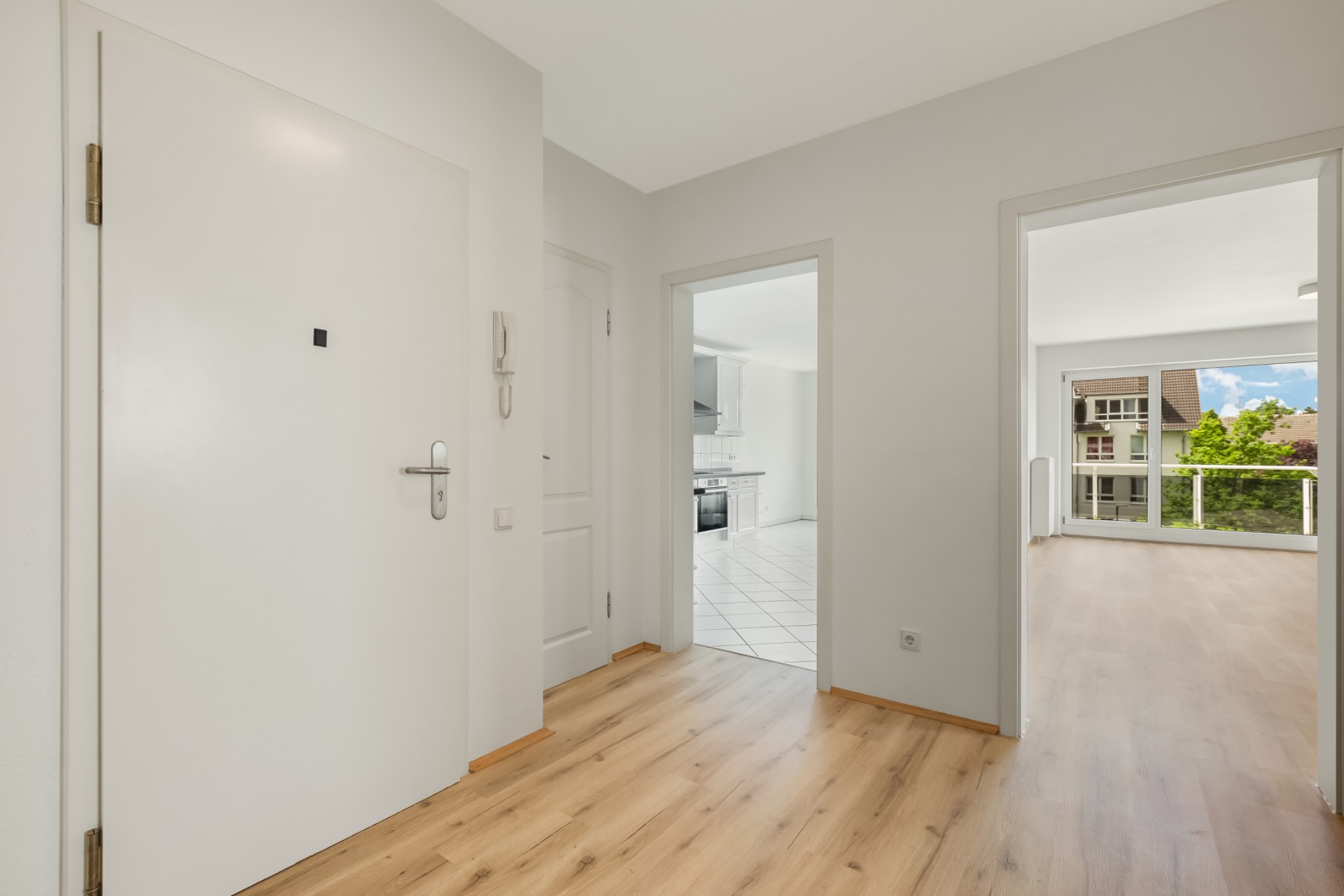 Flur mit Holzboden, Blick in Küche und Wohnzimmer mit großen Fenstern.