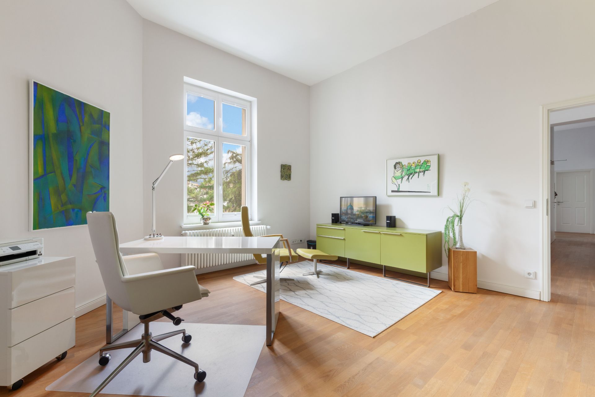 Helles Arbeitszimmer mit Schreibtisch, Stuhl, grünem Sideboard und großem Fenster.