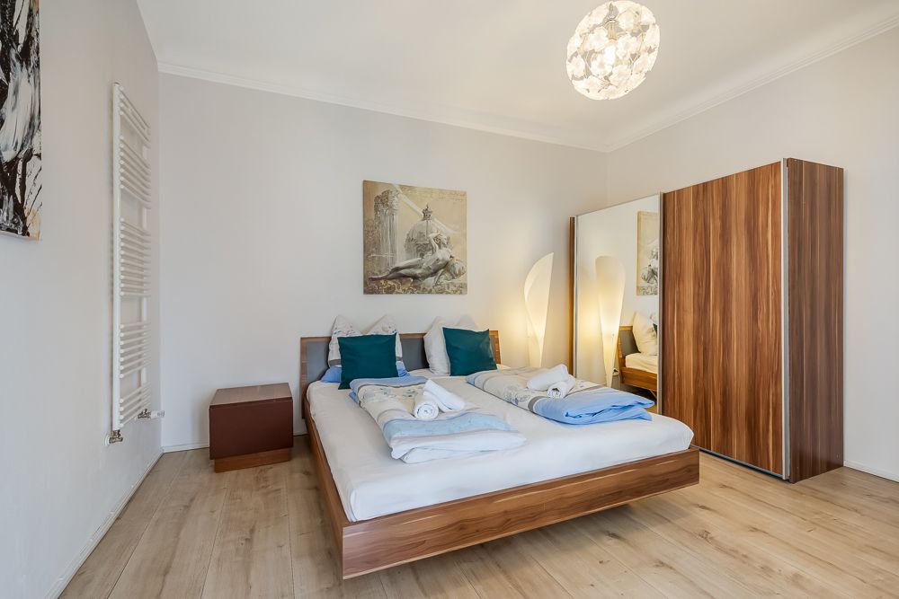 Helles Schlafzimmer mit Doppelbett, Holzschrank, Nachttisch und Stehlampe.