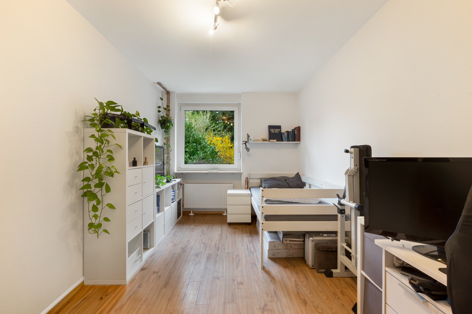 Helles Schlafzimmer mit Einzelbett, Regal, Schreibtisch und Fenster mit Blick ins Grüne.