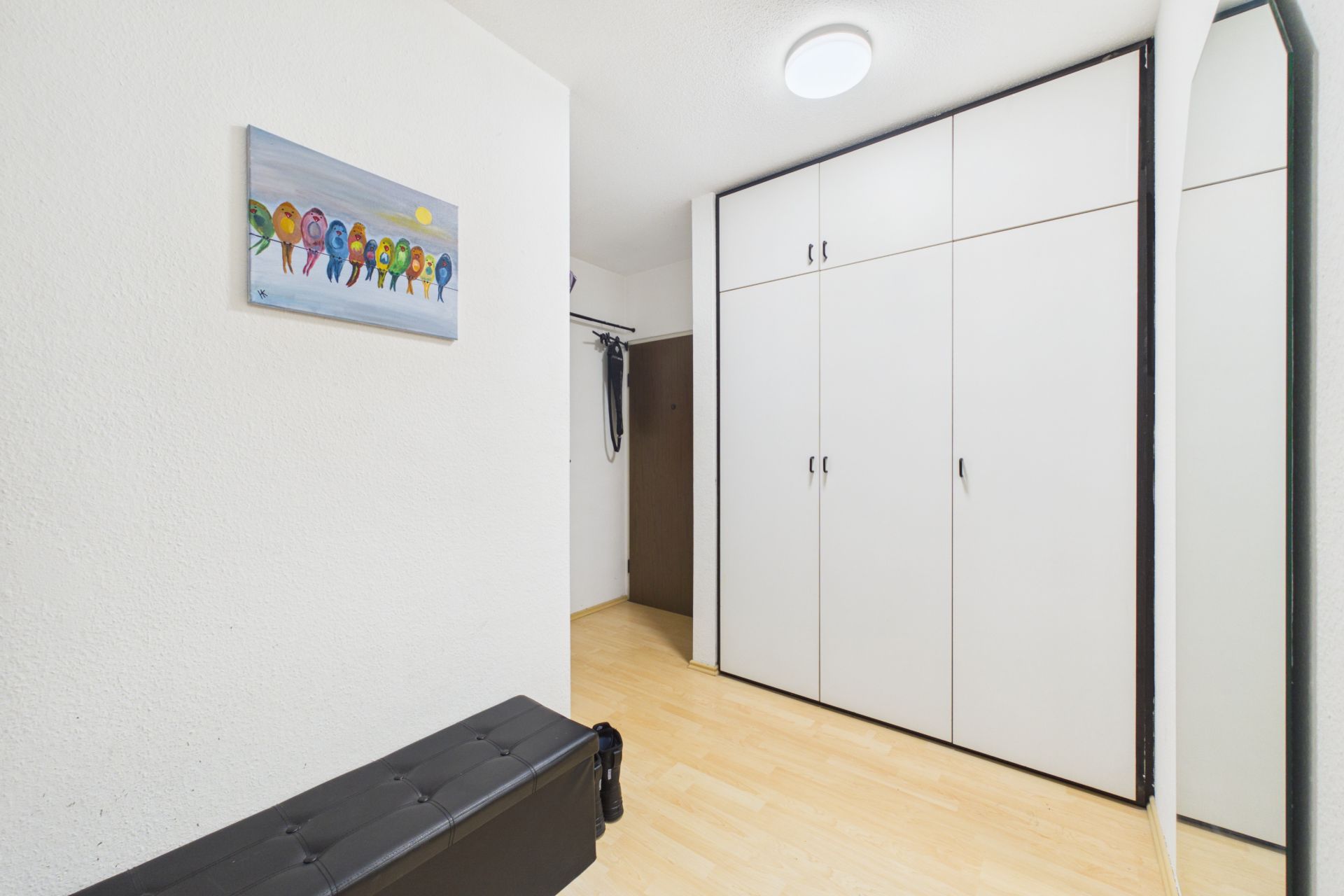 Flur mit großem weißen Einbauschrank, Spiegel, Bild und schwarzer Sitzbank.