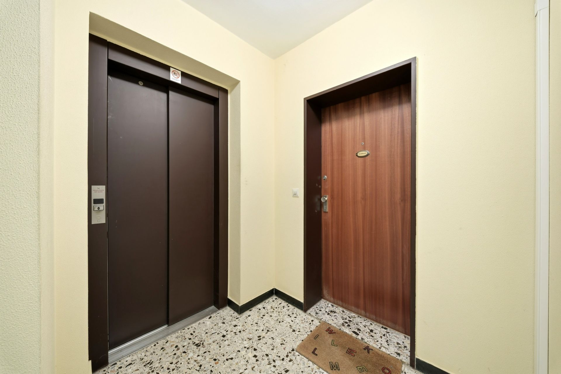 Flur mit Aufzug und Wohnungstür auf gemustertem Boden.