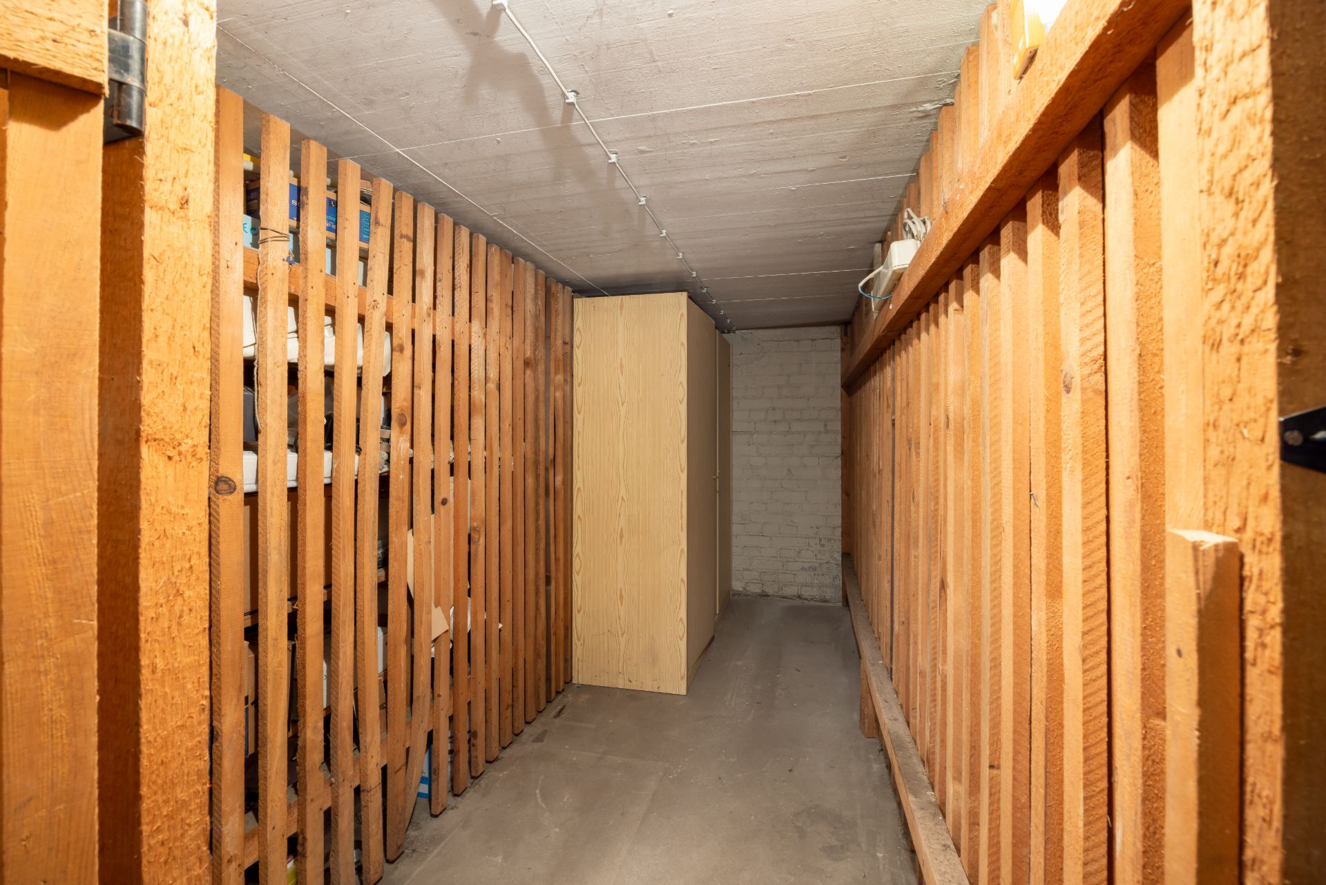 Schmaler Kellerraum mit Holzlattenwänden und einem Schrank an der Rückwand.