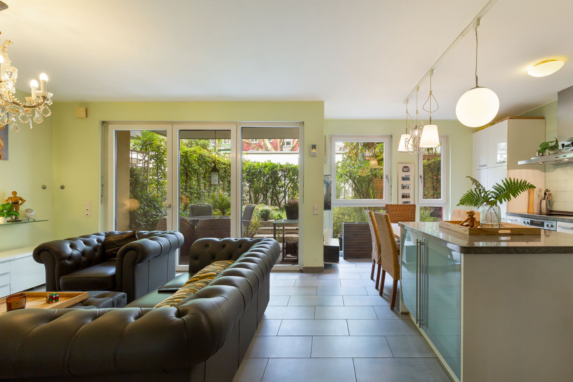 Modernes Wohnzimmer mit zwei Sofas, Essbereich und offener Küche. Große Fenster zeigen auf Garten.
