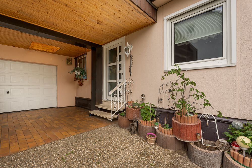 Überdachter Eingangsbereich mit Garage, Treppe, Pflanzgefäßen und einem Fenster.