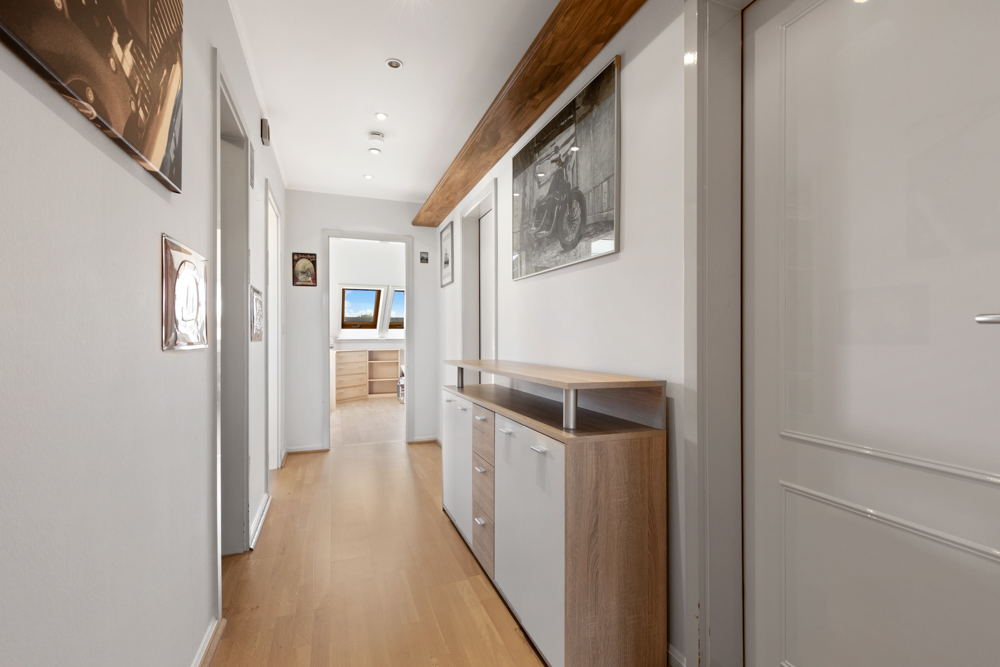 Heller Flur mit Holzfußboden, Kommode und Wandbildern, im Hintergrund ein Zimmer mit Dachfenstern.