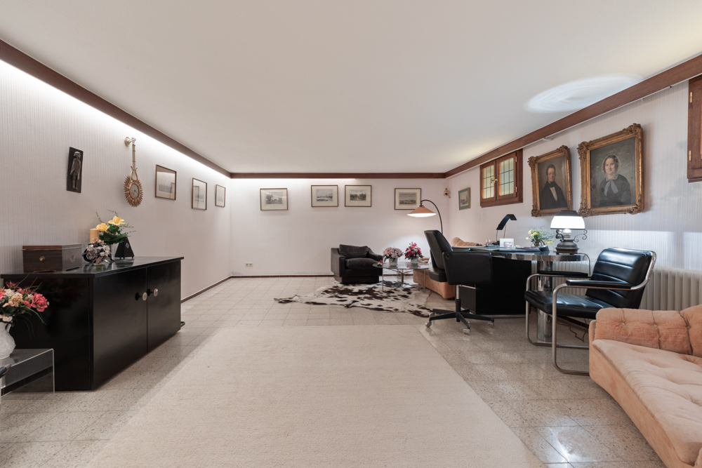 Wohnzimmer mit mehreren Sesseln, Schreibtisch, Kommode und Bildern an den Wänden.