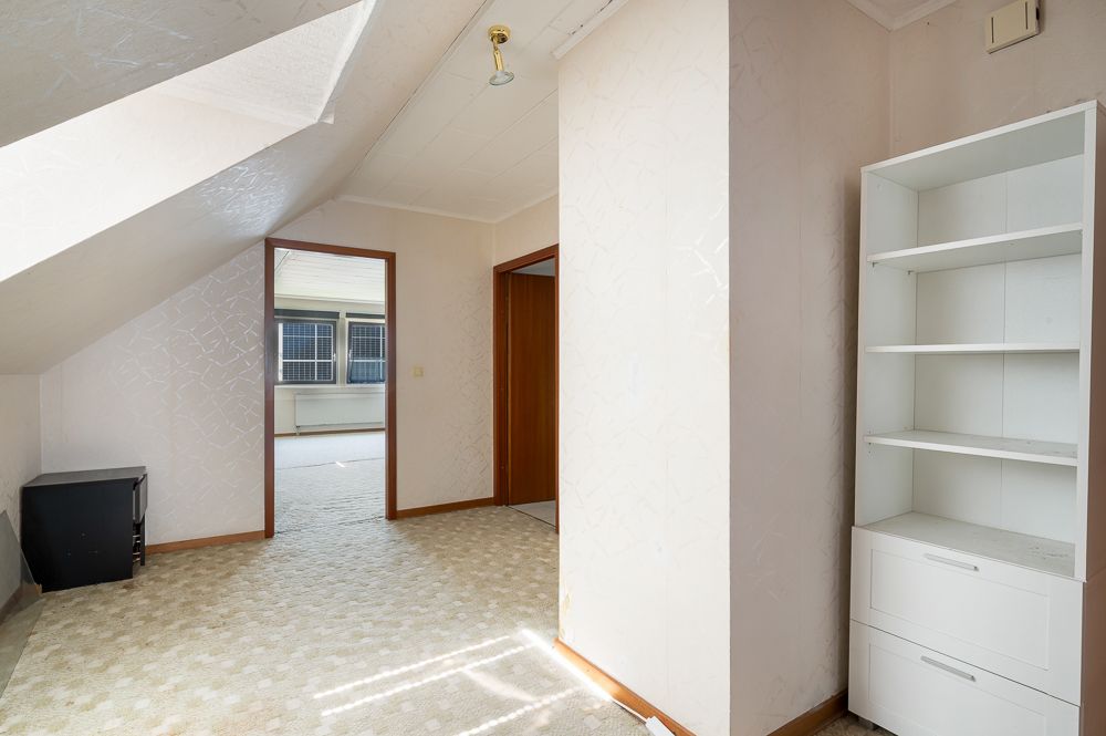 Zimmer mit Dachschräge, Teppichboden, weißem Regal und zwei offenen Türen.