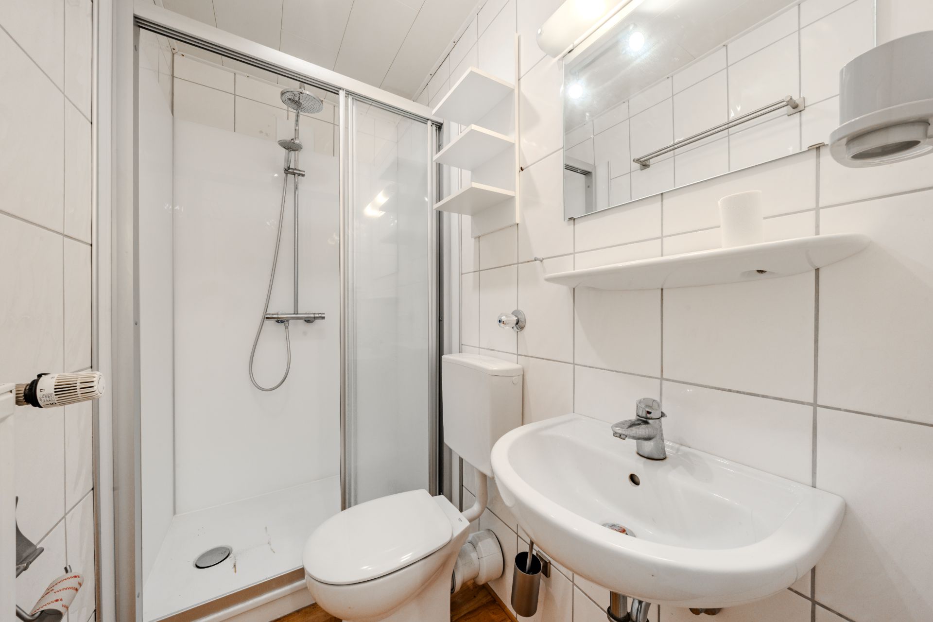 Kleines Bad mit Dusche, WC, Waschbecken, Spiegel und weißen Fliesen.