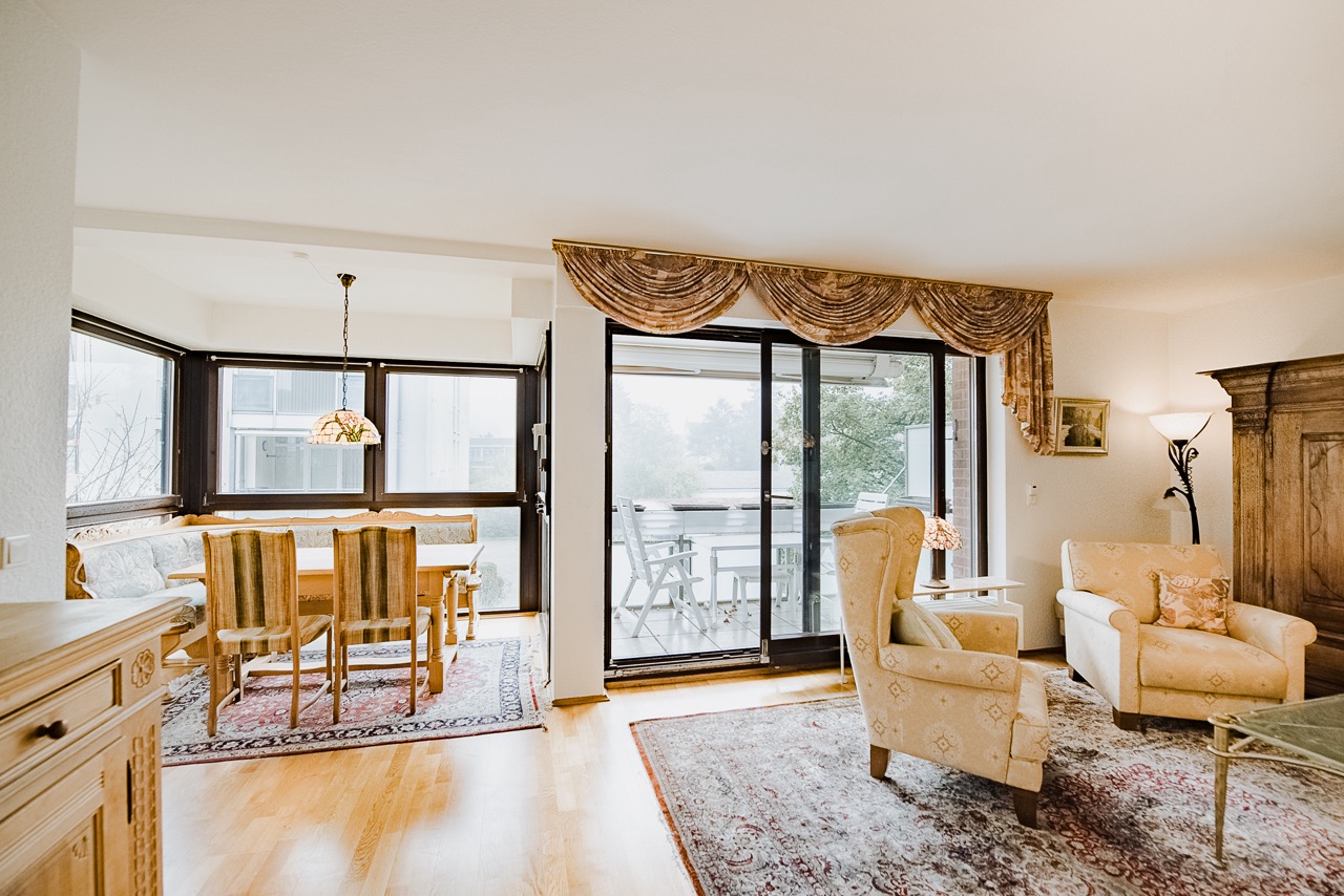 Helles Wohnzimmer mit Esstisch, Stühlen, Sofa, Sesseln und Zugang zum Balkon.