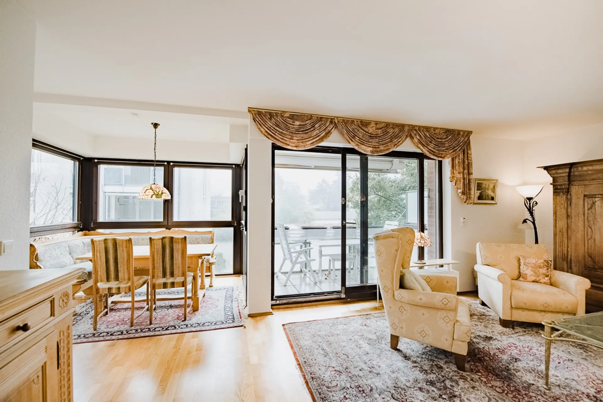 Helles Wohnzimmer mit Esstisch, Stühlen, Sofa, Sesseln und Zugang zum Balkon.