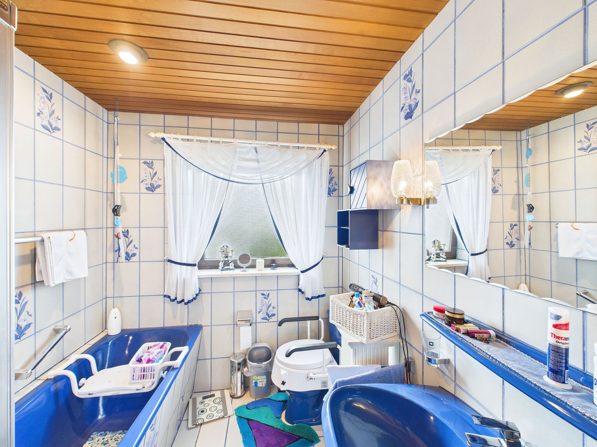 Badezimmer mit blauen Sanitäranlagen, weißen Fliesen und einem Fenster mit Vorhängen.