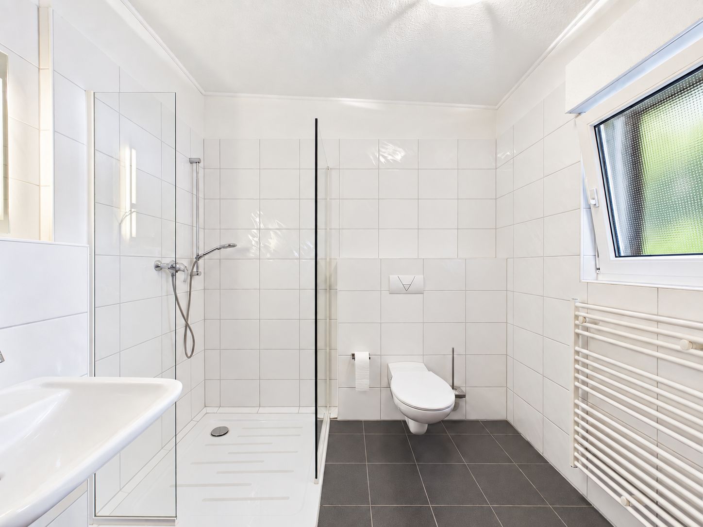 Modernes Bad mit bodengleicher Dusche, Wand-WC, Waschbecken und Fenster.
