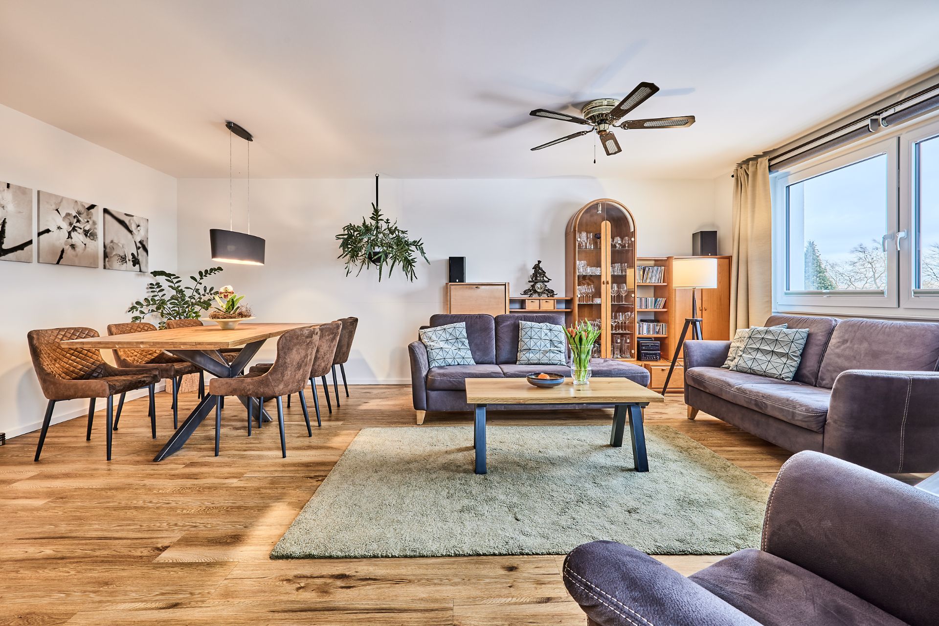 Modernes Wohnzimmer mit Essbereich, Holzboden, Sofas, Esstisch und großen Fenstern.