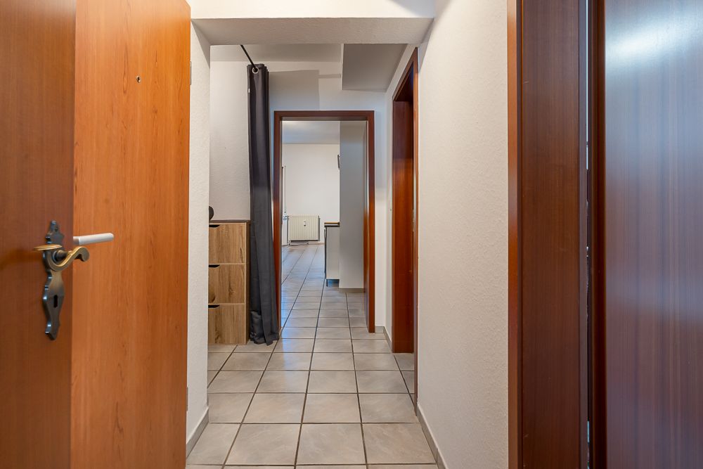 Heller Flur mit Fliesenboden und Holztüren, Blick in ein weiteres Zimmer.