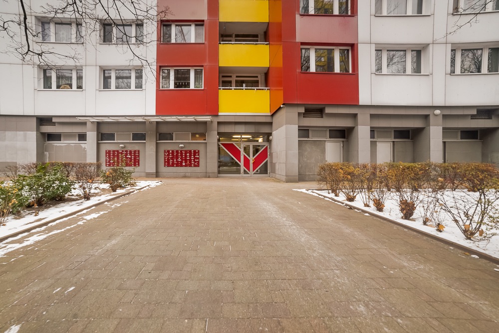 Eingang eines Wohnhauses mit bunten Fassaden und Briefkästen, Weg mit etwas Schnee.