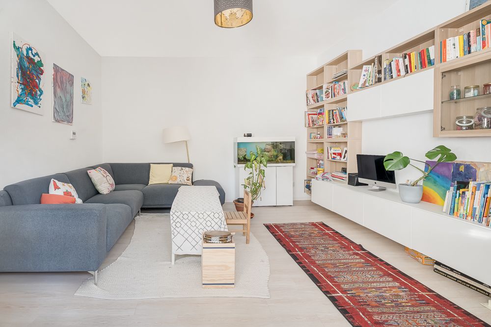 Helles Wohnzimmer mit grauem Sofa, Bücherregalen, Aquarium und Teppich.