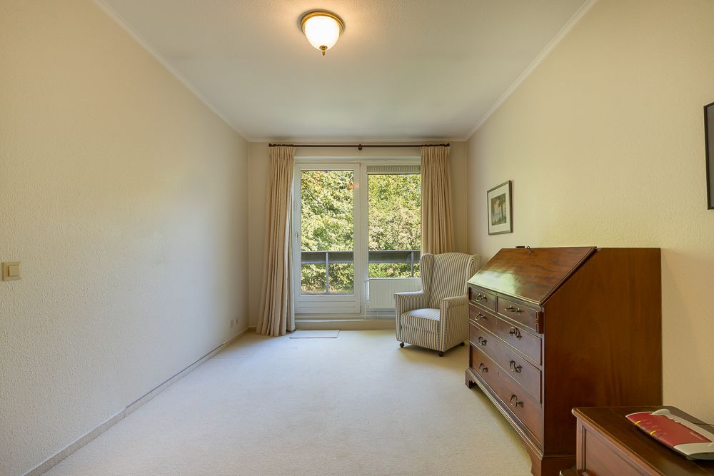 Helles Zimmer mit Sessel, Schreibtisch, Kommode und Fenster mit Blick ins Grüne.