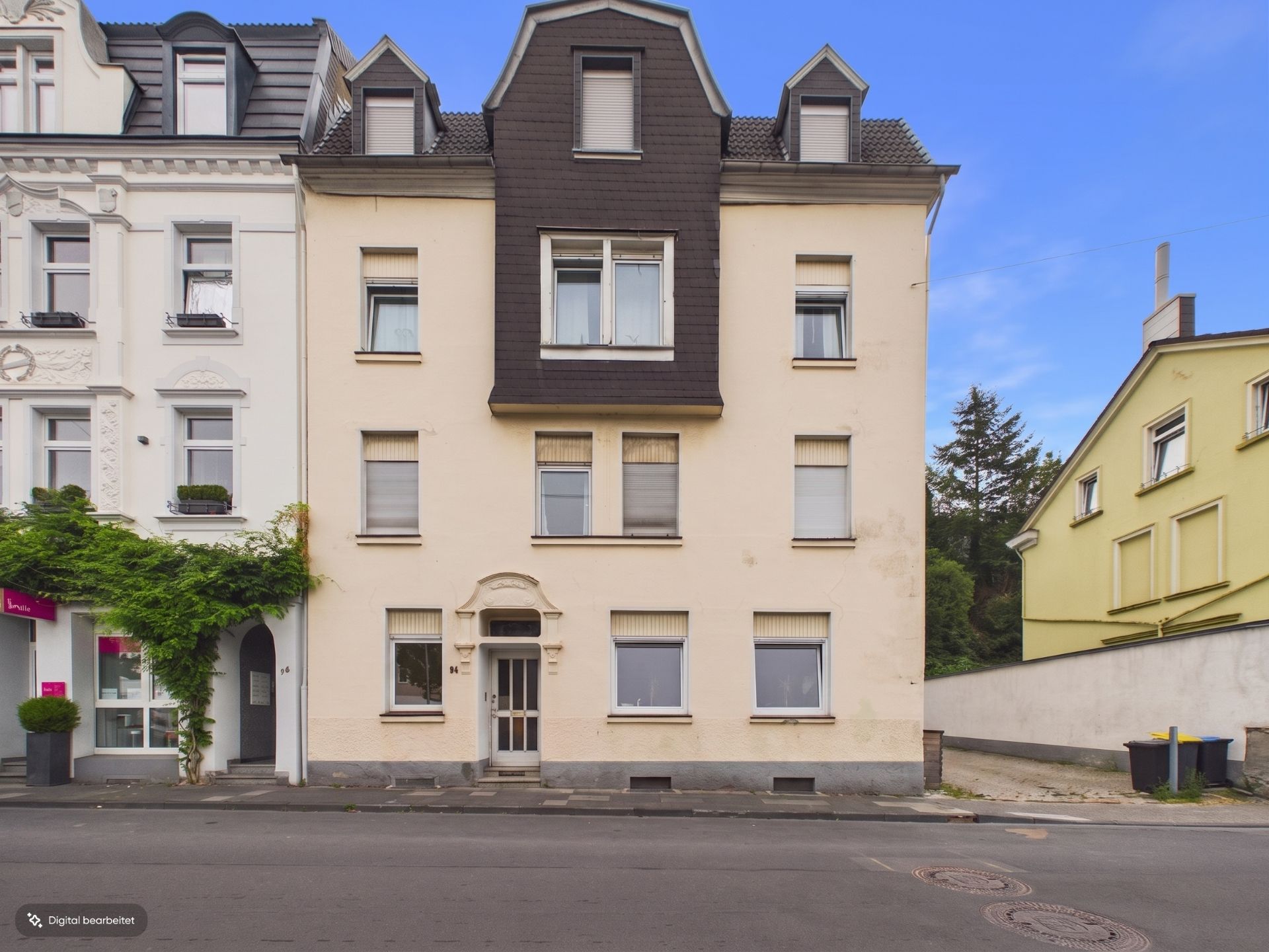 Vorderansicht eines mehrstöckigen Wohnhauses mit hellbeiger Fassade und mehreren Fenstern.