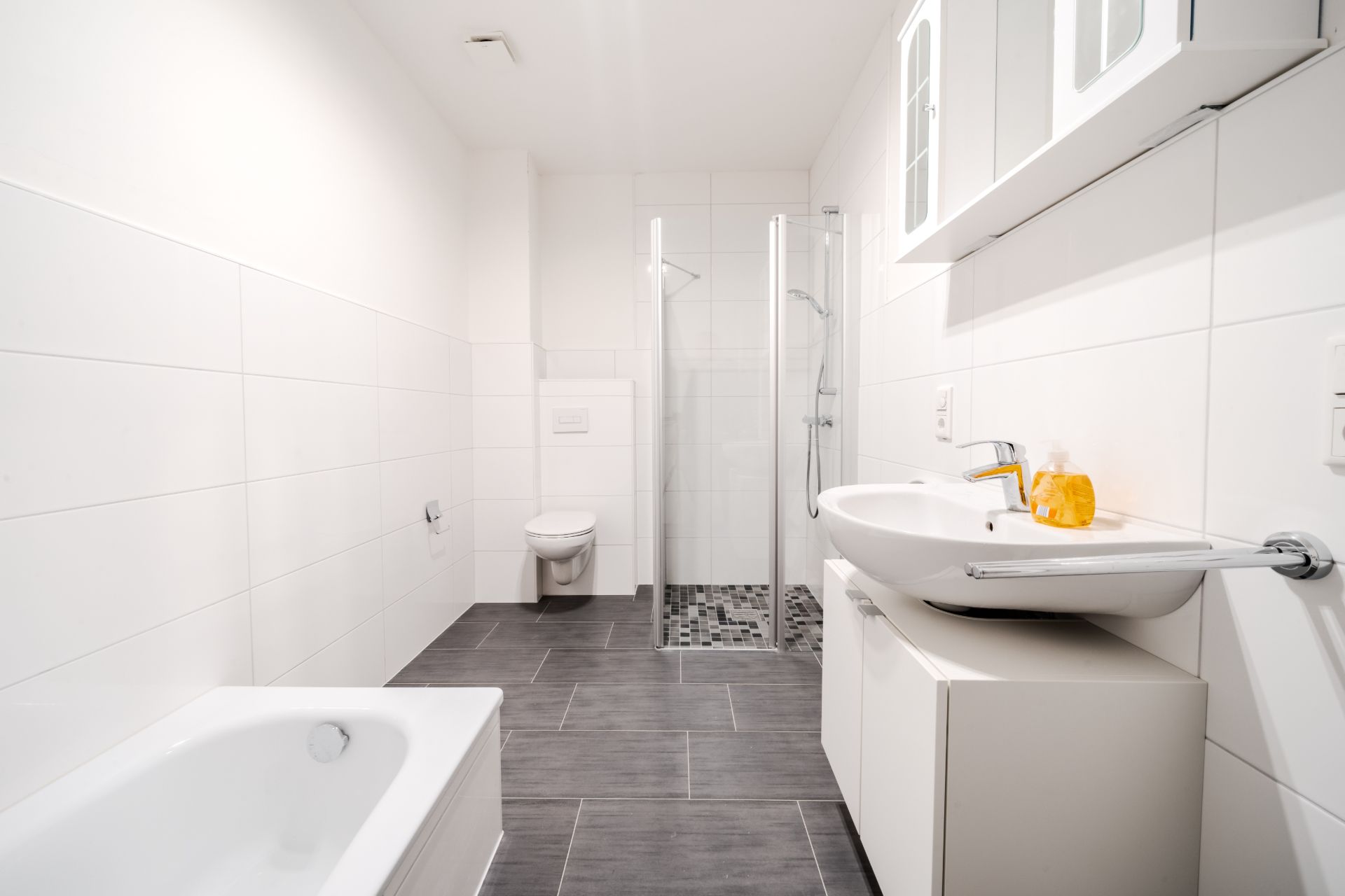 Modernes, weiß gefliestes Badezimmer mit Dusche, Badewanne, Toilette und Waschbecken.