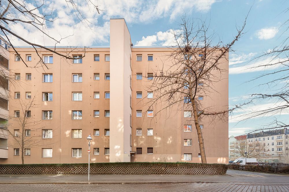 Mehrstöckiges Wohnhaus mit vielen Fenstern und kahlen Bäumen davor.
