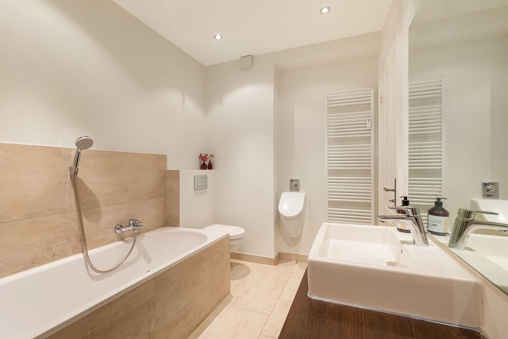 Modernes Badezimmer mit Badewanne, Waschbecken, Toilette, Urinal und Handtuchheizkörper.