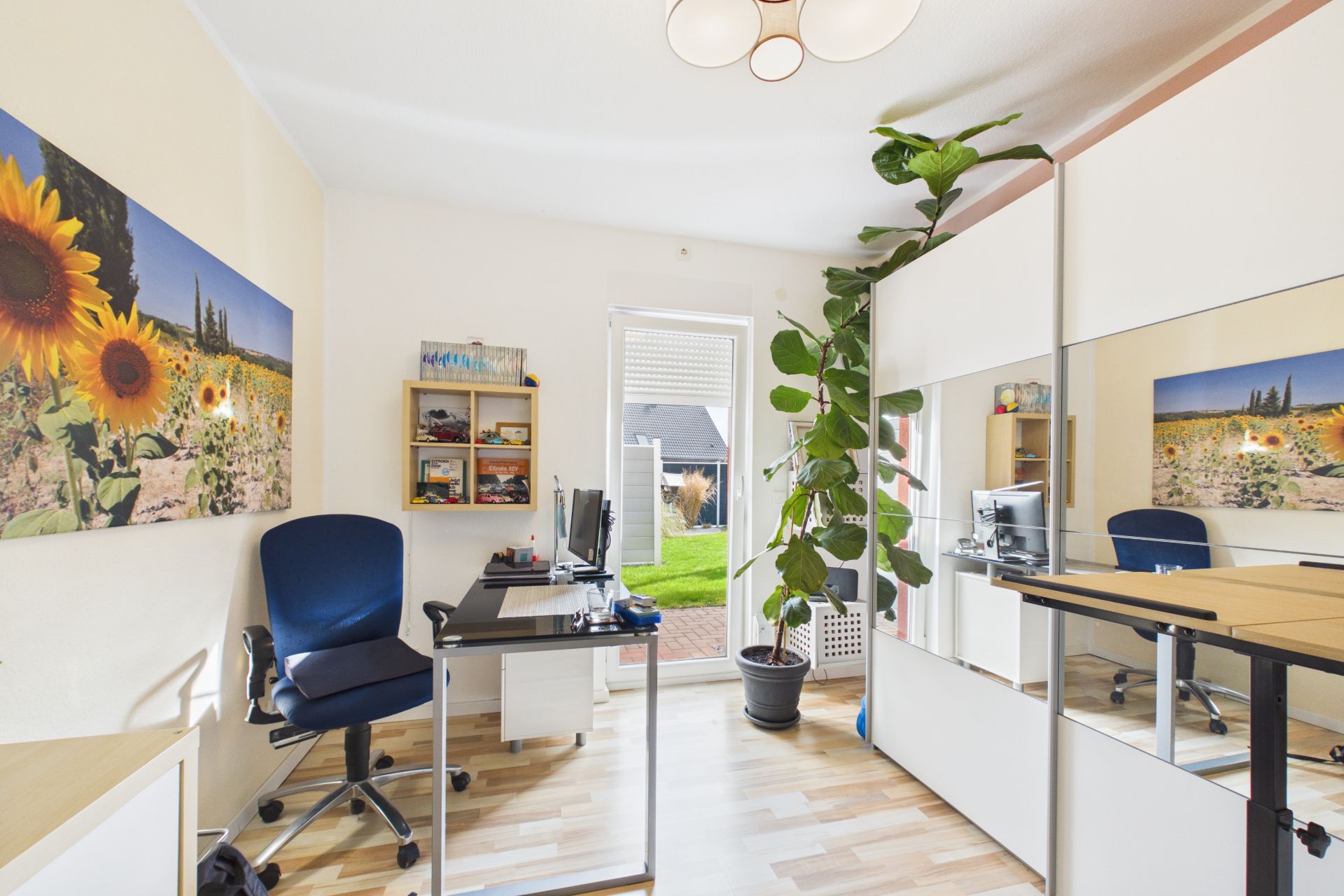 Helles Arbeitszimmer mit Schreibtisch, Bürostuhl, großem Spiegel und einer Zimmerpflanze.