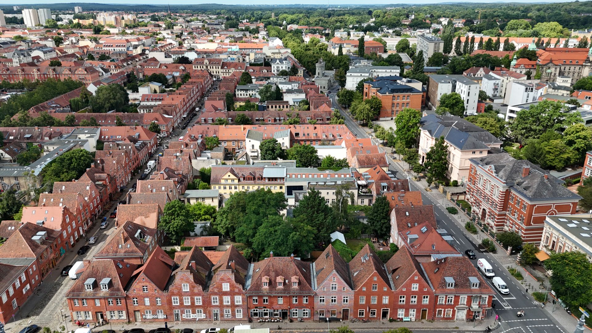 Luftaufnahme von roten Wohnhäusern mit Satteldächern in einer grünen Stadtgegend.