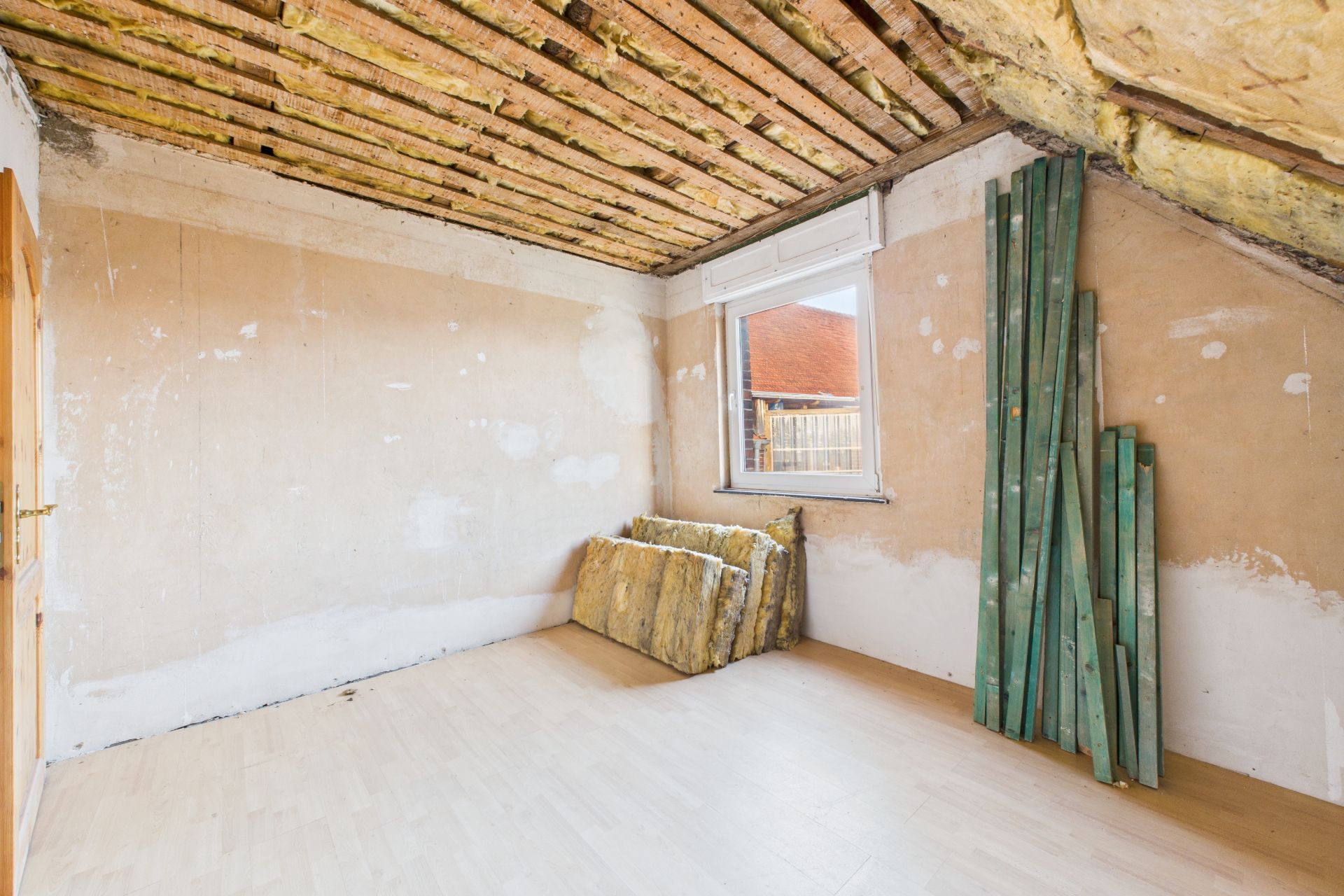Leerer Raum mit unfertiger Decke, gelagerten Holzlatten und Dämmmaterial an der Wand.
