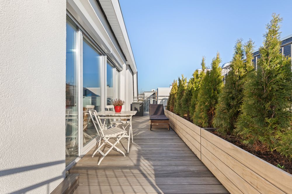 Große Dachterrasse mit Holzboden, Gartenmöbeln und Pflanzkübeln mit grünen Sträuchern.