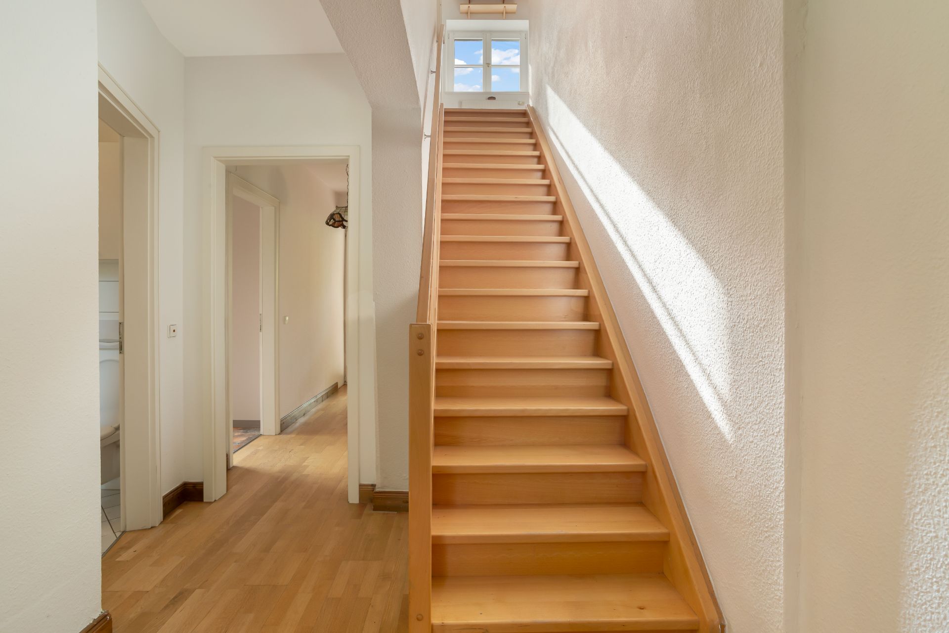 Heller Flur mit Holztreppe und Türen zu angrenzenden Zimmern.