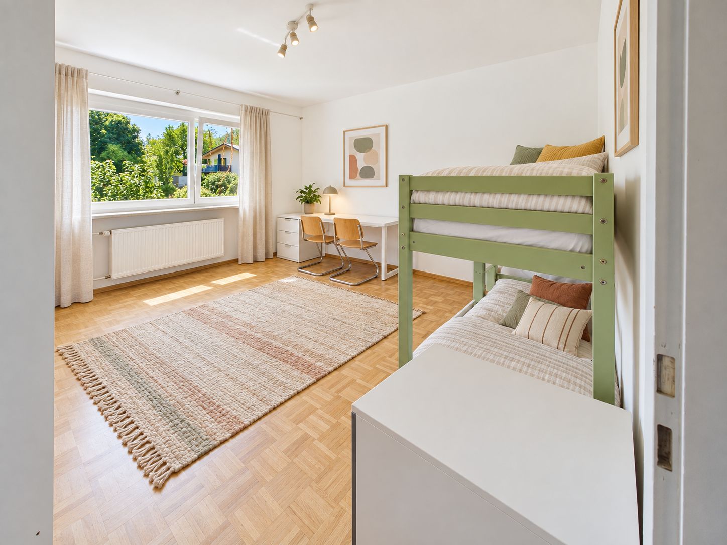 Helles Zimmer mit Etagenbett, Schreibtisch, zwei Stühlen und großem Fenster mit Blick ins Grüne.