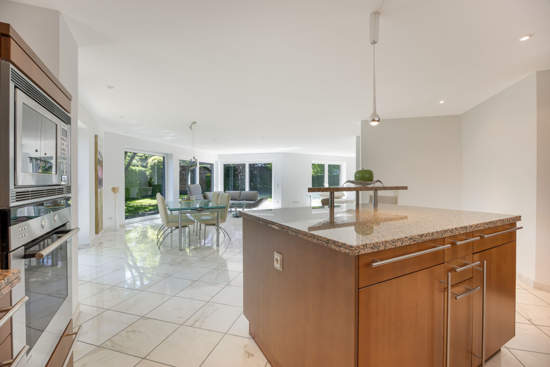 Moderne Küche mit Kochinsel, Essbereich und Wohnzimmer mit großen Fenstern zum Garten.
