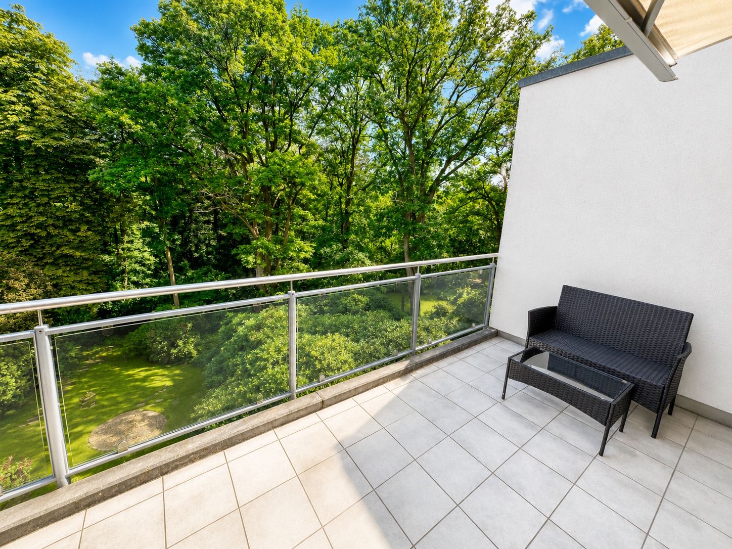 Helle Terrasse mit Sitzbank und Glängeländer, Blick auf grüne Bäume.