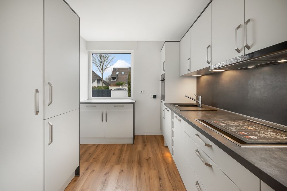 Helle, moderne Küche mit weißen Schränken, Holzboden und großem Fenster.