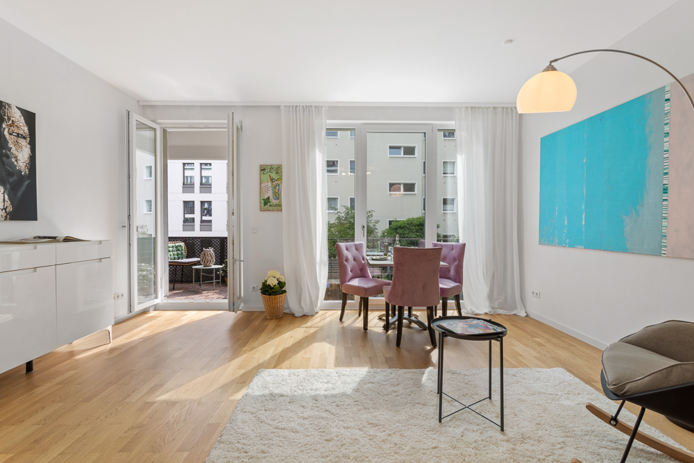 Helles Wohnzimmer mit Essbereich, großen Fenstern und Zugang zu einem Balkon.