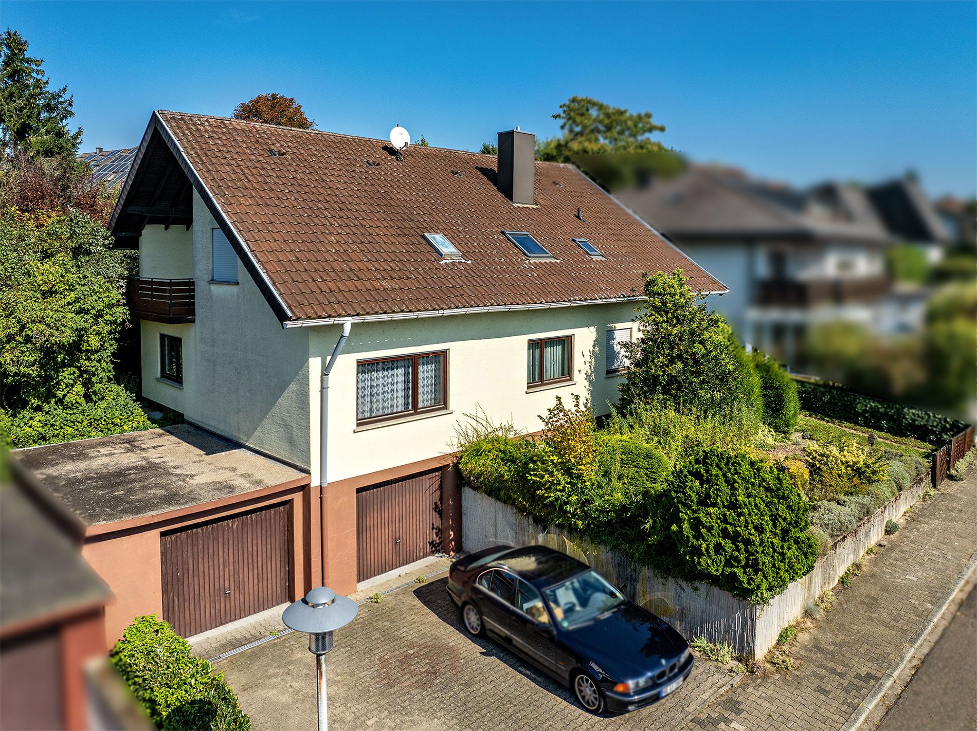 Einfamilienhaus mit braunem Dach, Garage, Auto und vorgelagertem Garten an einer Straße.
