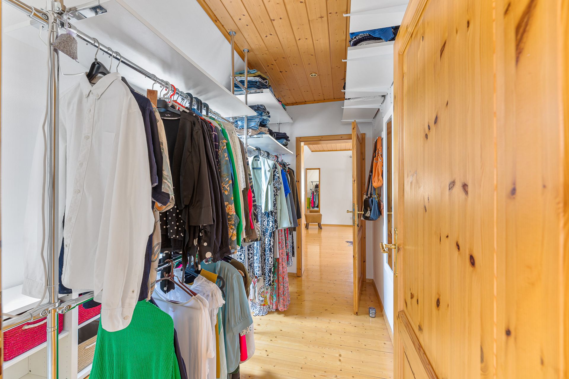 Schmaler begehbarer Kleiderschrank mit hängender Kleidung und Holzdecke.